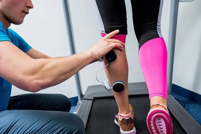 A man is examining a woman 's leg on a treadmill.