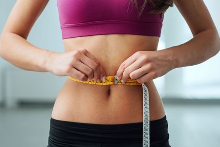 A woman is measuring her waist with a tape measure.