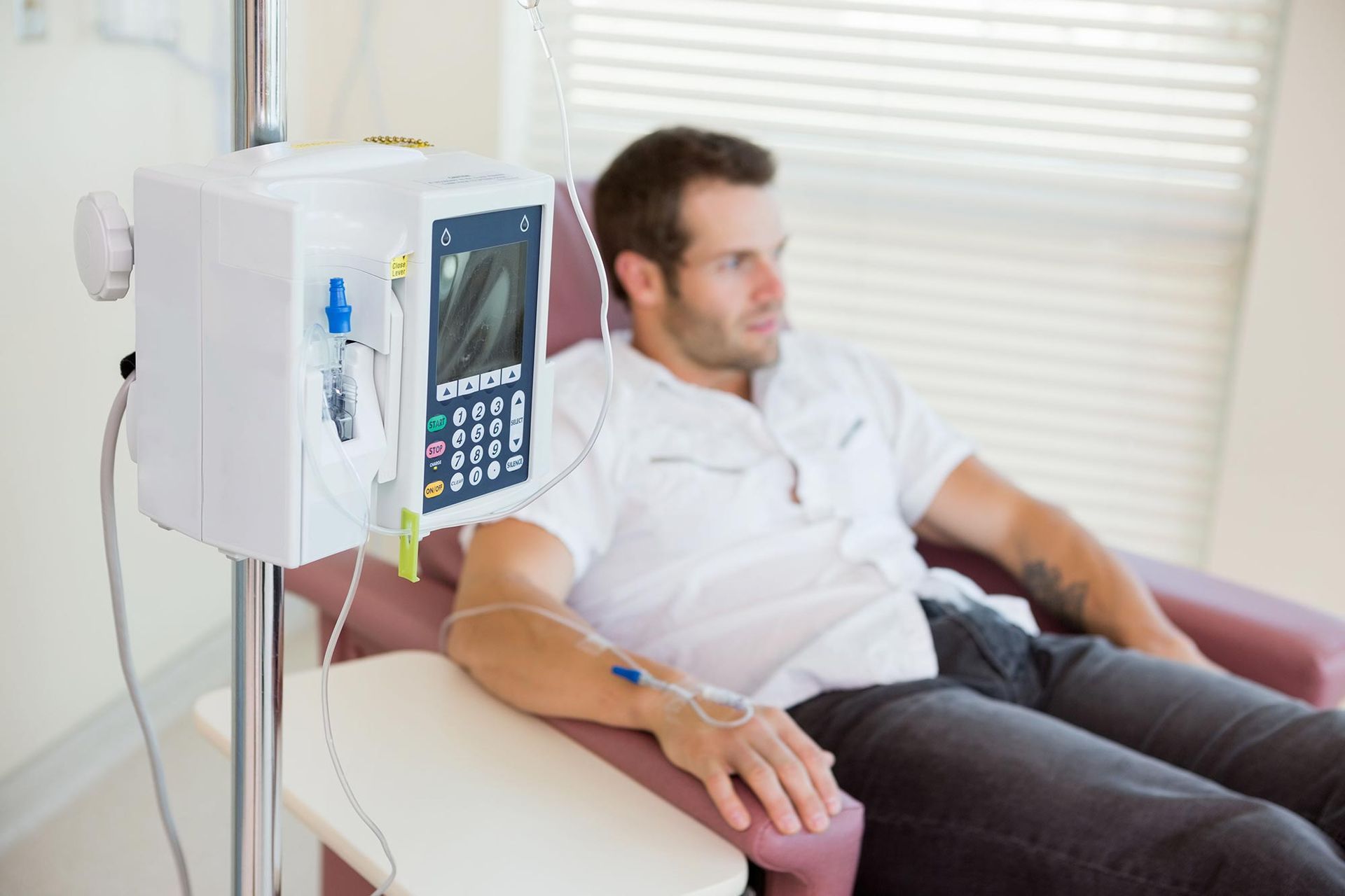Man receiving IV treatment, sitting in a chair next to medical equipment in a bright room.