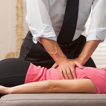 A woman in a pink shirt is laying on a table getting a massage from a man in a tie.