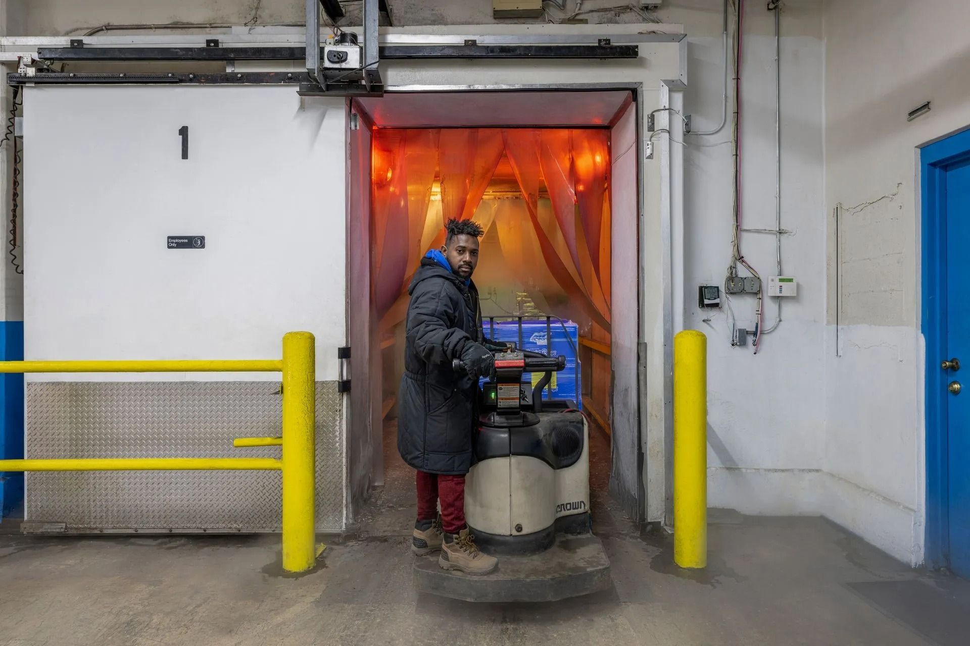 Man on an electric pallet jack inside a loading dock with blue boxes.