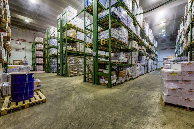 Warehouse interior with tall shelving packed with boxes. A blue barrel sits on a pallet in the foreground.