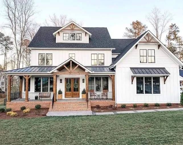 White farmhouse with dark roof, brick porch, and wooden accents.