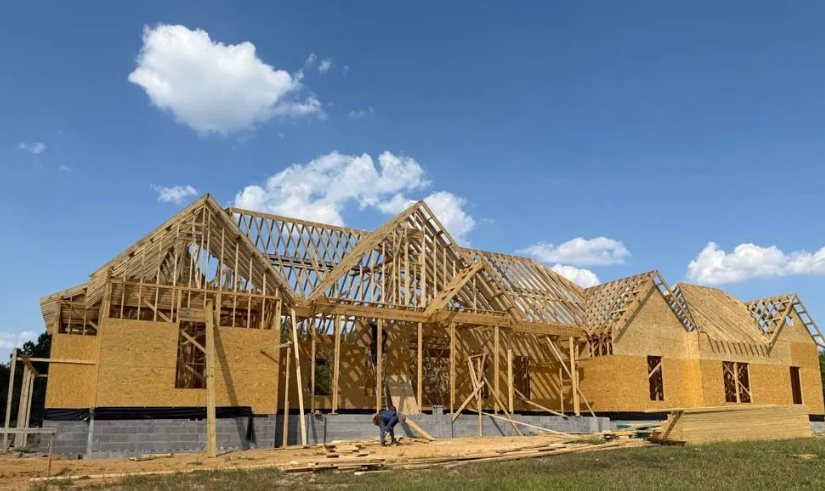 Construction of a new house, wooden framework visible against a blue sky, worker on site.
