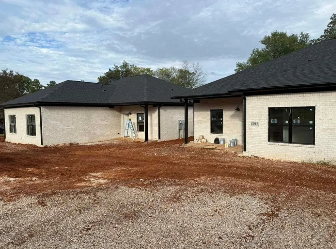 New construction houses with white brick, black trim and roof, on a dirt lot.