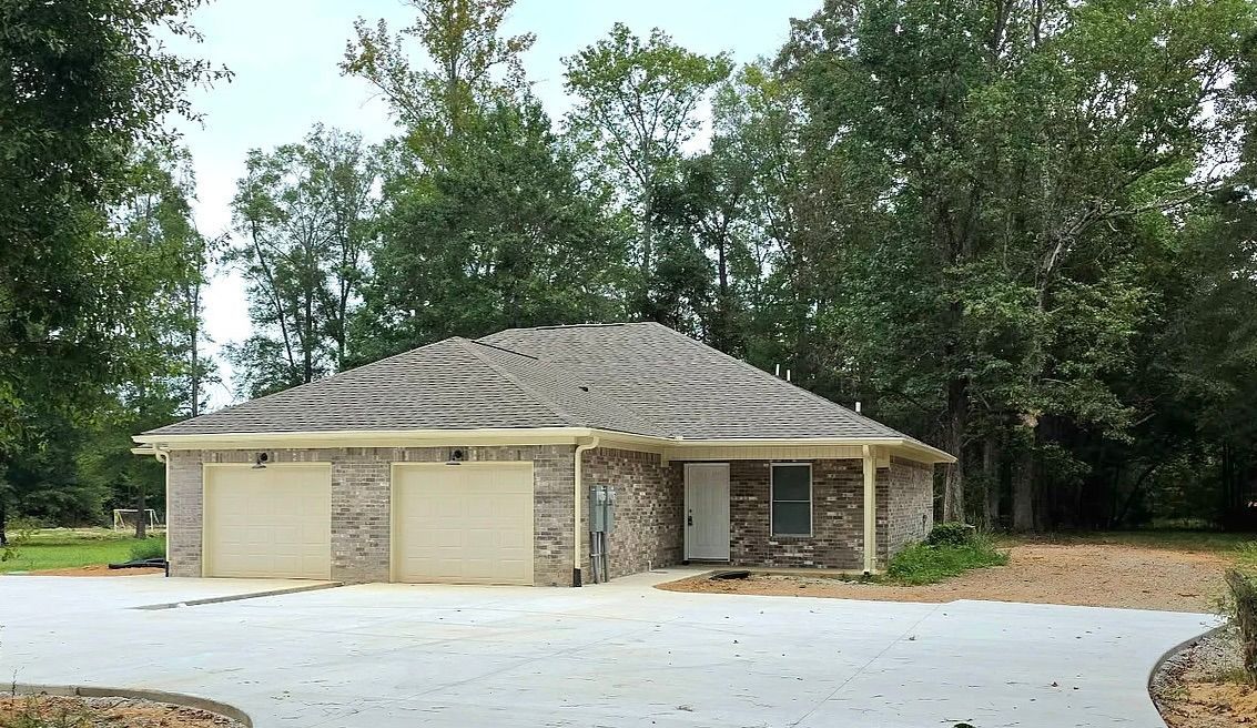 Brick home with a two-car garage, surrounded by trees and a concrete driveway.
