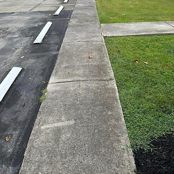 A sidewalk next to a parking lot and a grassy area