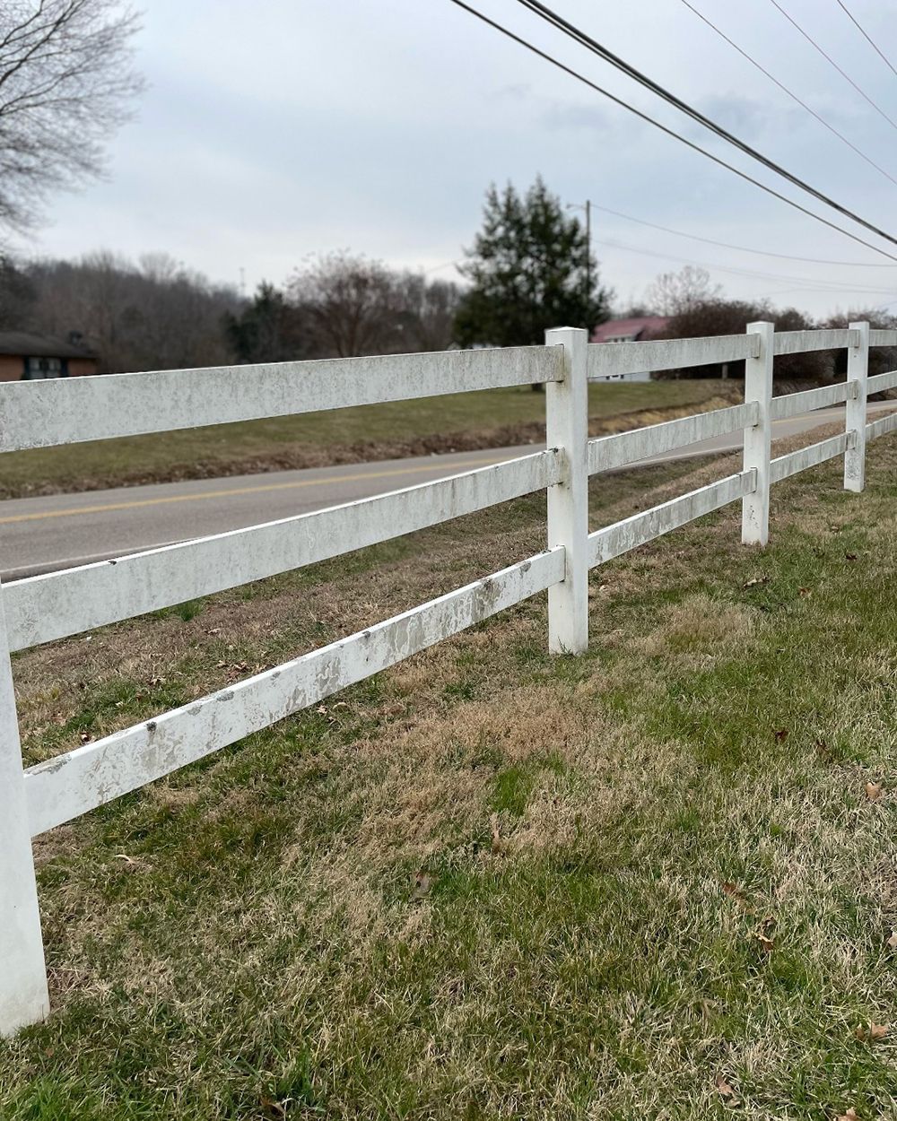 A white fence surrounds a grassy field next to a road