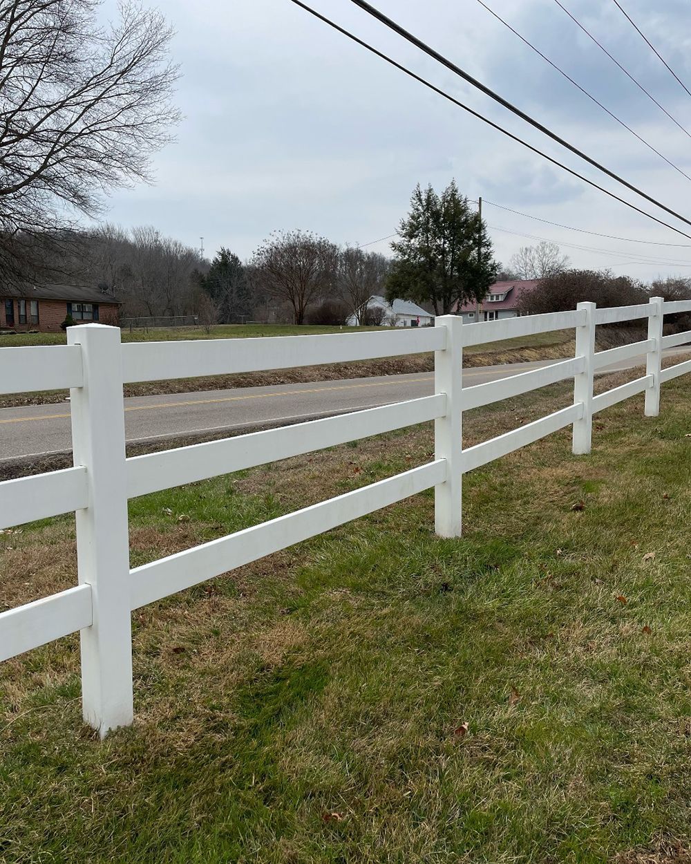 A white fence surrounds a grassy field next to a road