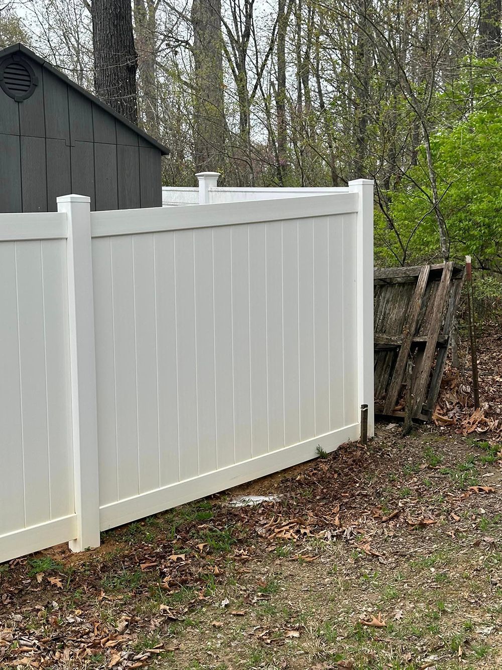 A white fence is sitting in the middle of a yard next to a shed