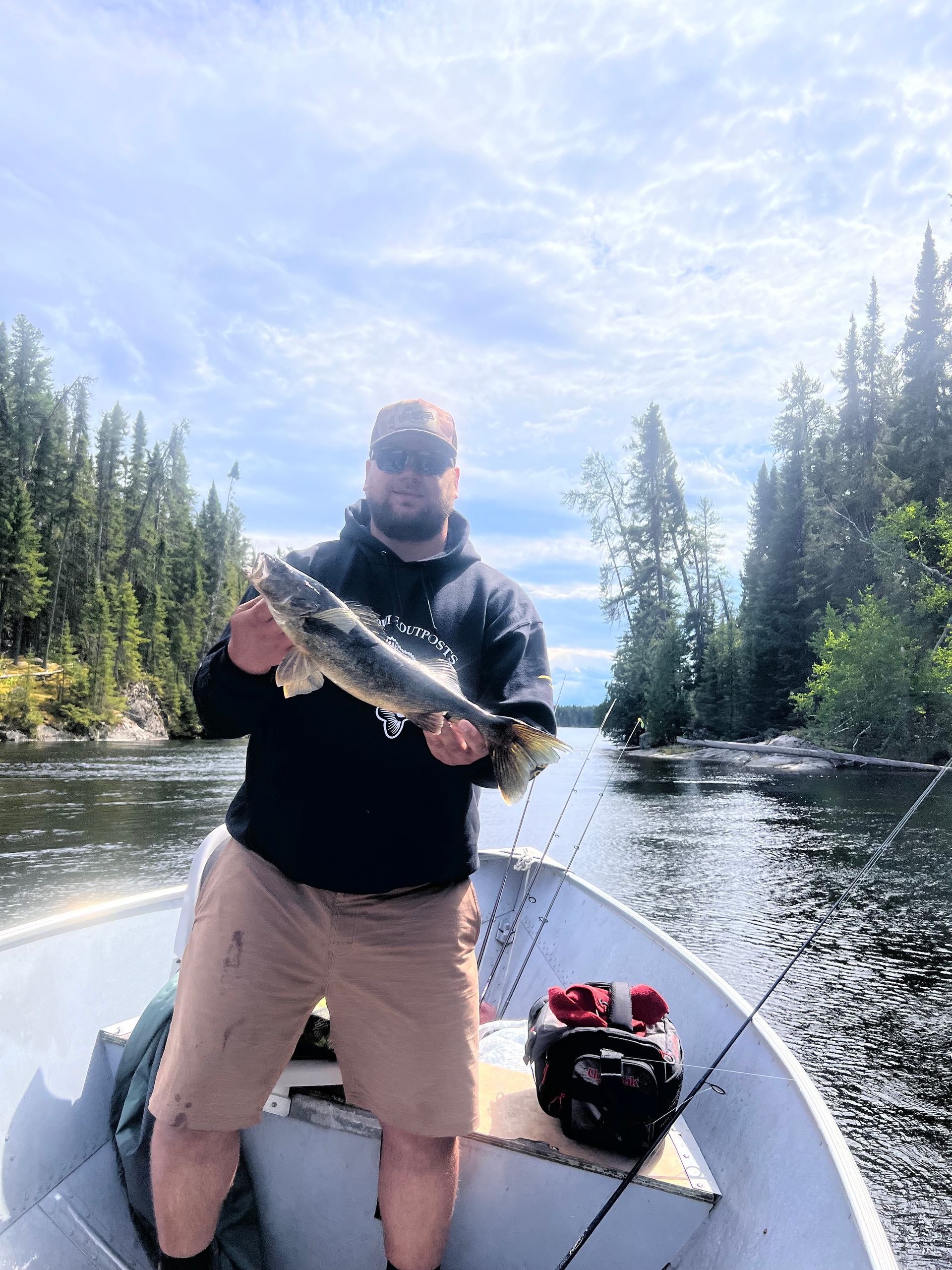 Person holding a fish on a canoe in a forested river, with another fish and gear on board