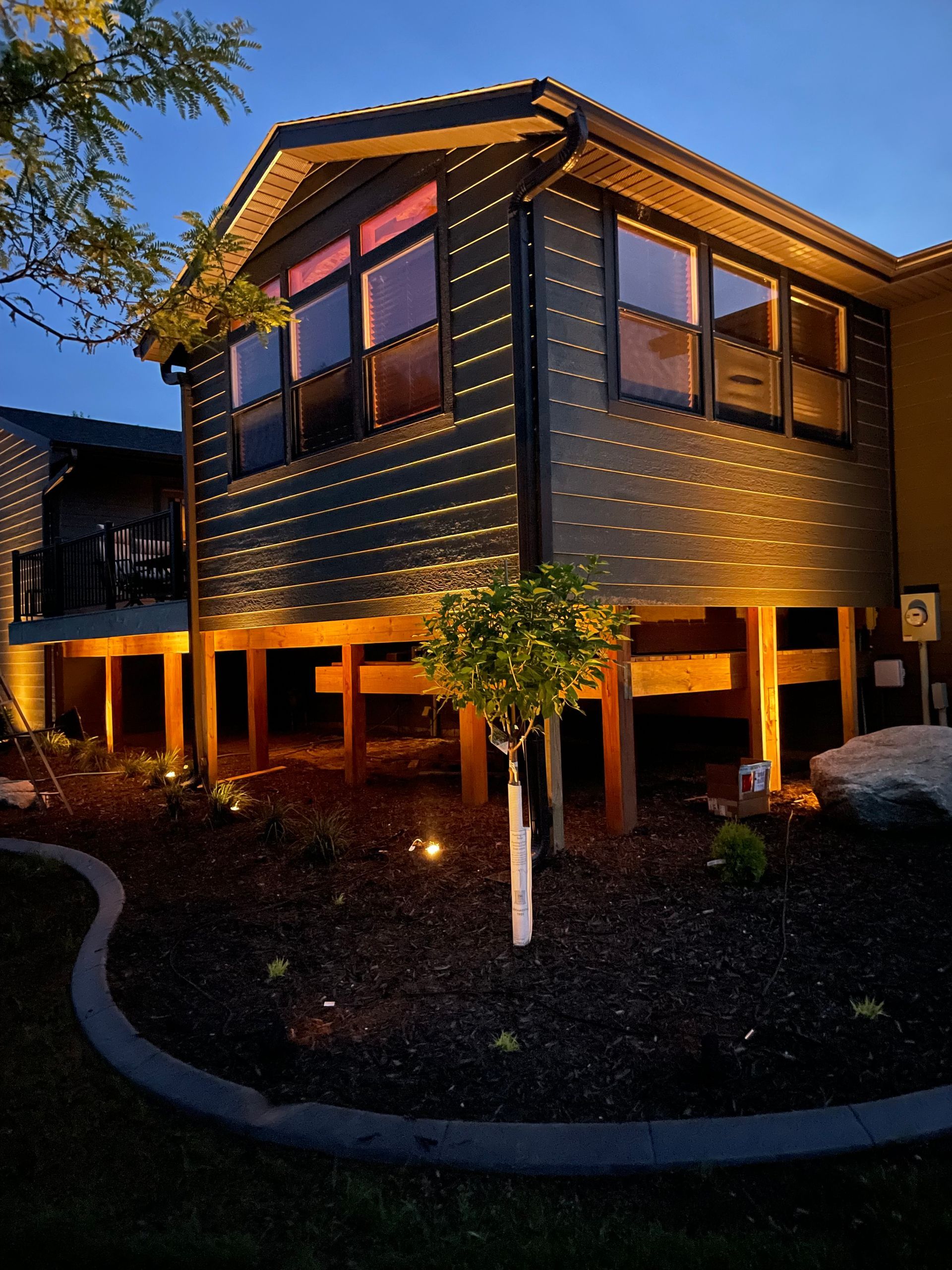 Modern two-story house with warm exterior lighting at dusk, surrounded by landscaped garden and driveway