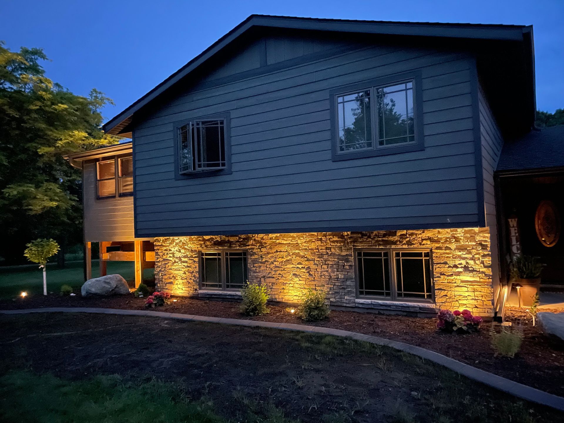 Two-story house at dusk with stone-lit lower facade and dark blue siding