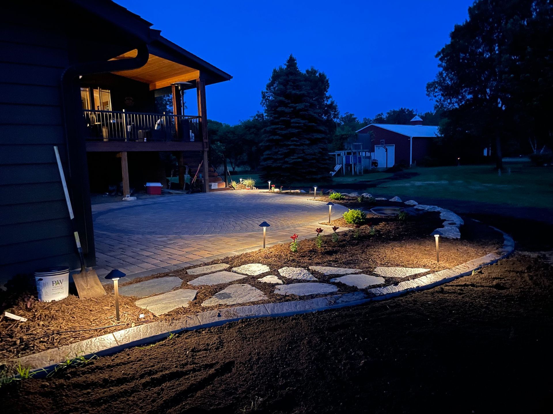 Nighttime backyard with lit stone path, landscaped garden bed, and house deck under blue sky