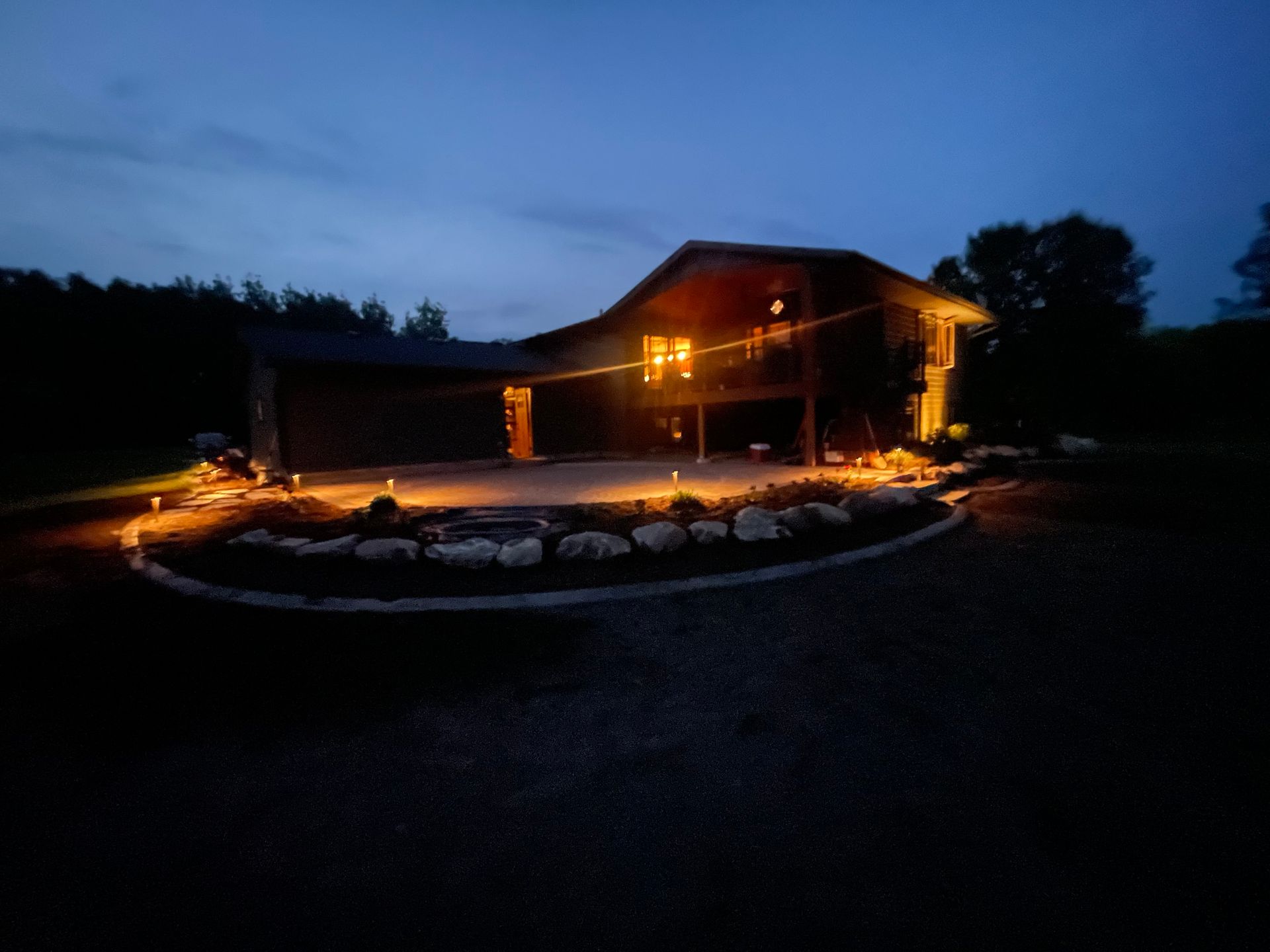 Log cabin at dusk with warm lights, stone fire pit, and glowing curved walkway in front.