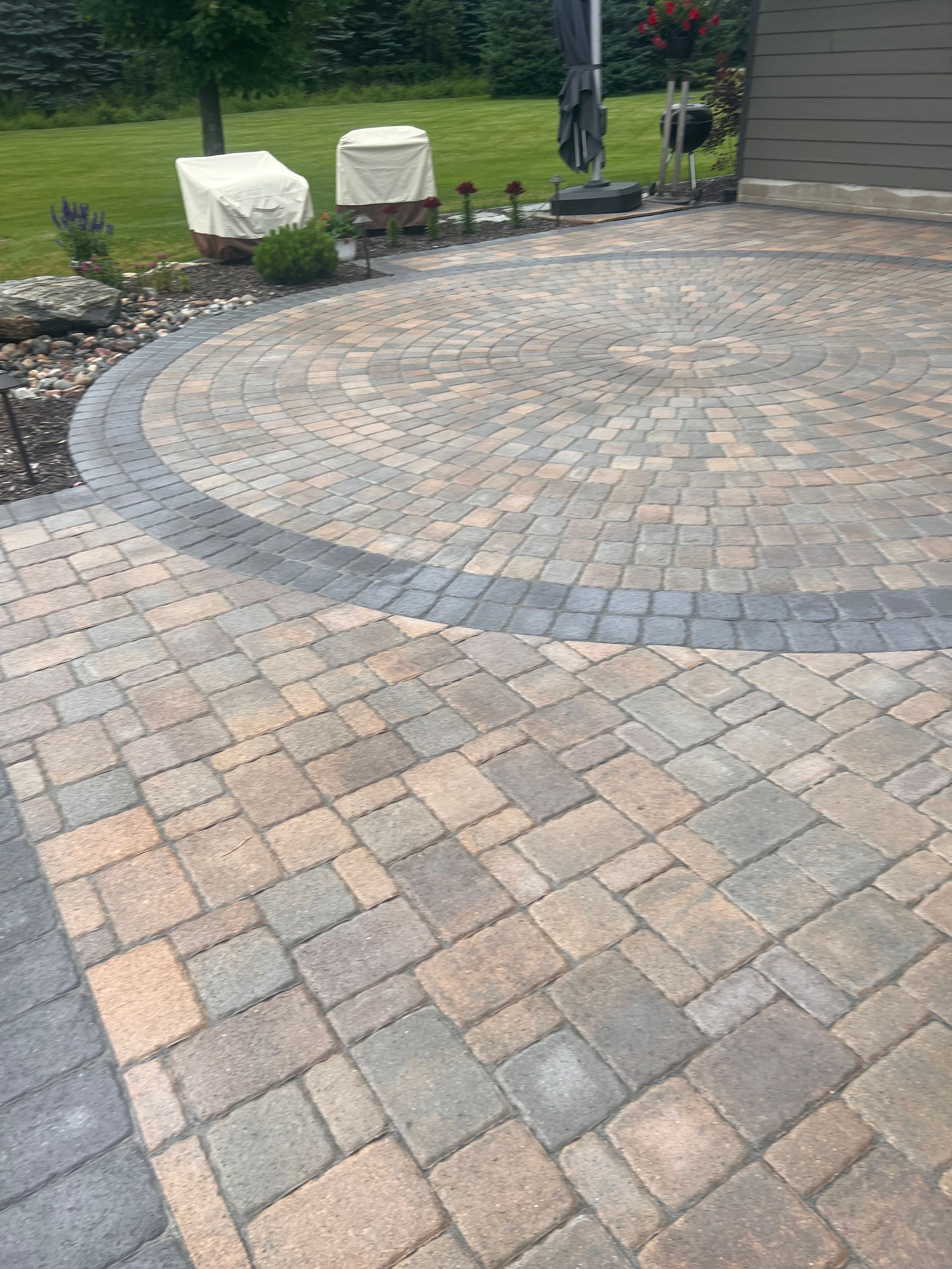 Curved gray and tan stone paver patio in a backyard garden area