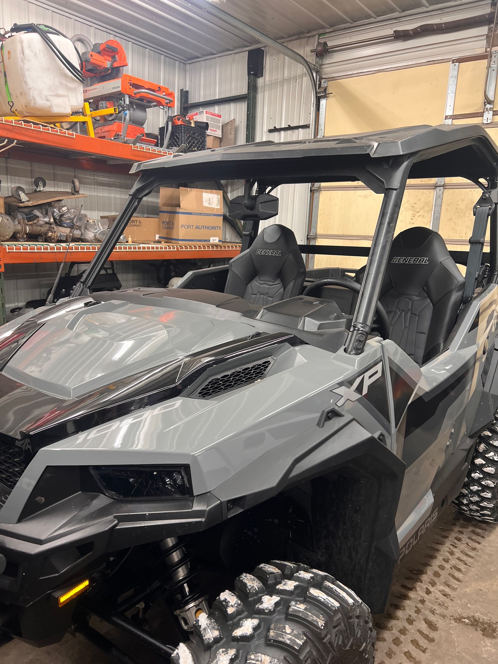 Gray off-road side-by-side UTV parked inside a garage with shelves and tools in the background