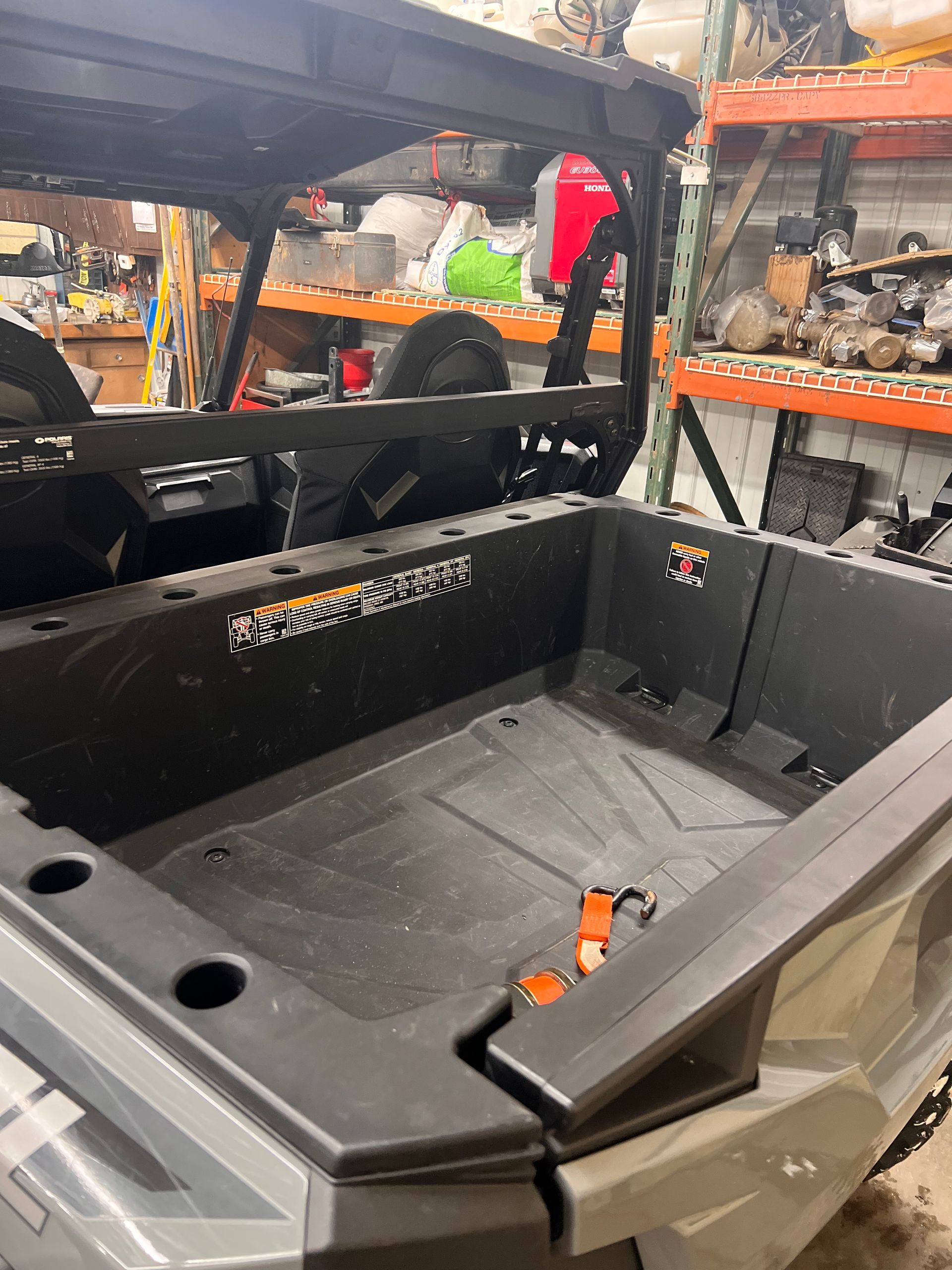 Black utility vehicle cargo bed inside a workshop, with gray side panels and orange latches.
