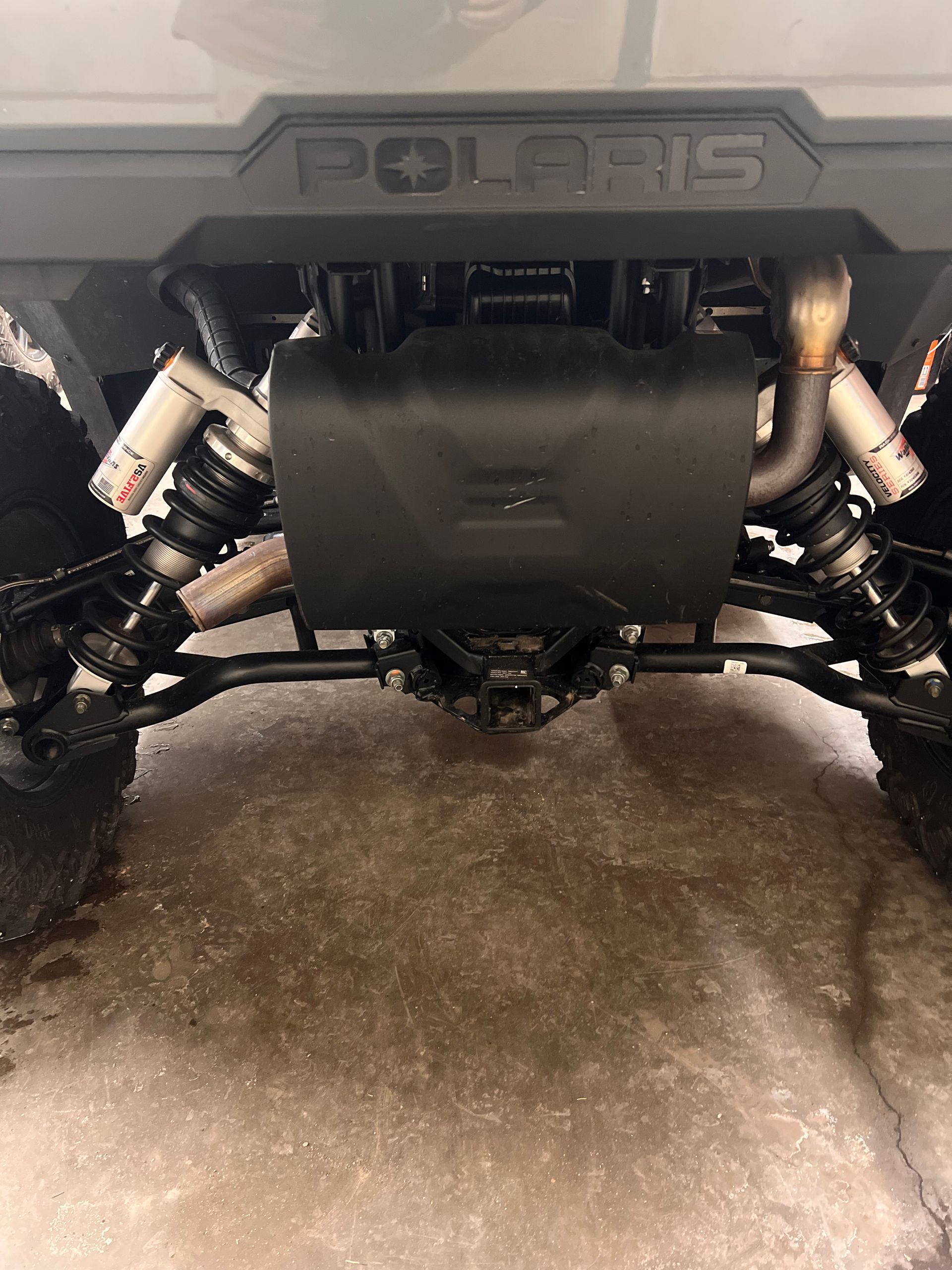 Undercarriage view of an off-road vehicle with suspension and a skid plate above wet ground