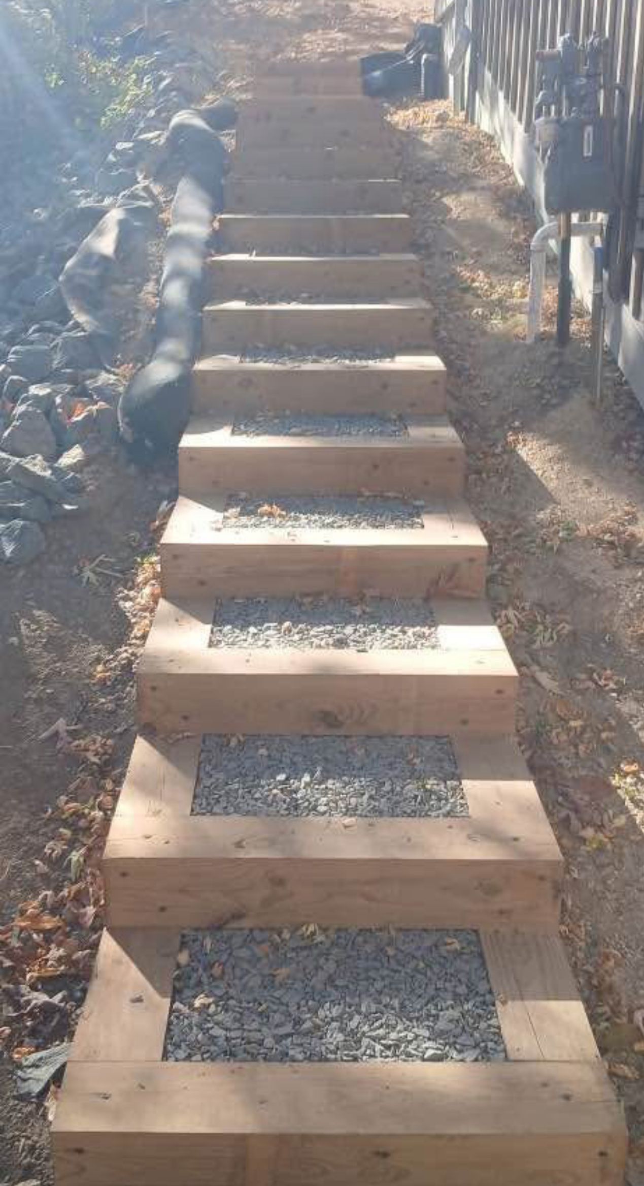 Wooden outdoor staircase with gravel-filled steps leading uphill between fences and dirt sides