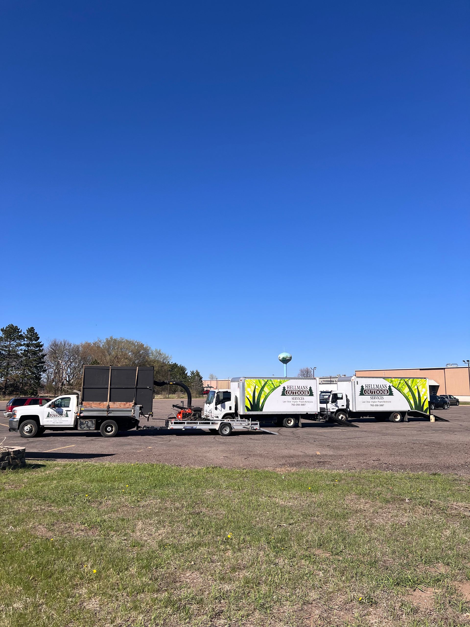 Work trucks and trailers parked on a grassy lot under a clear blue sky