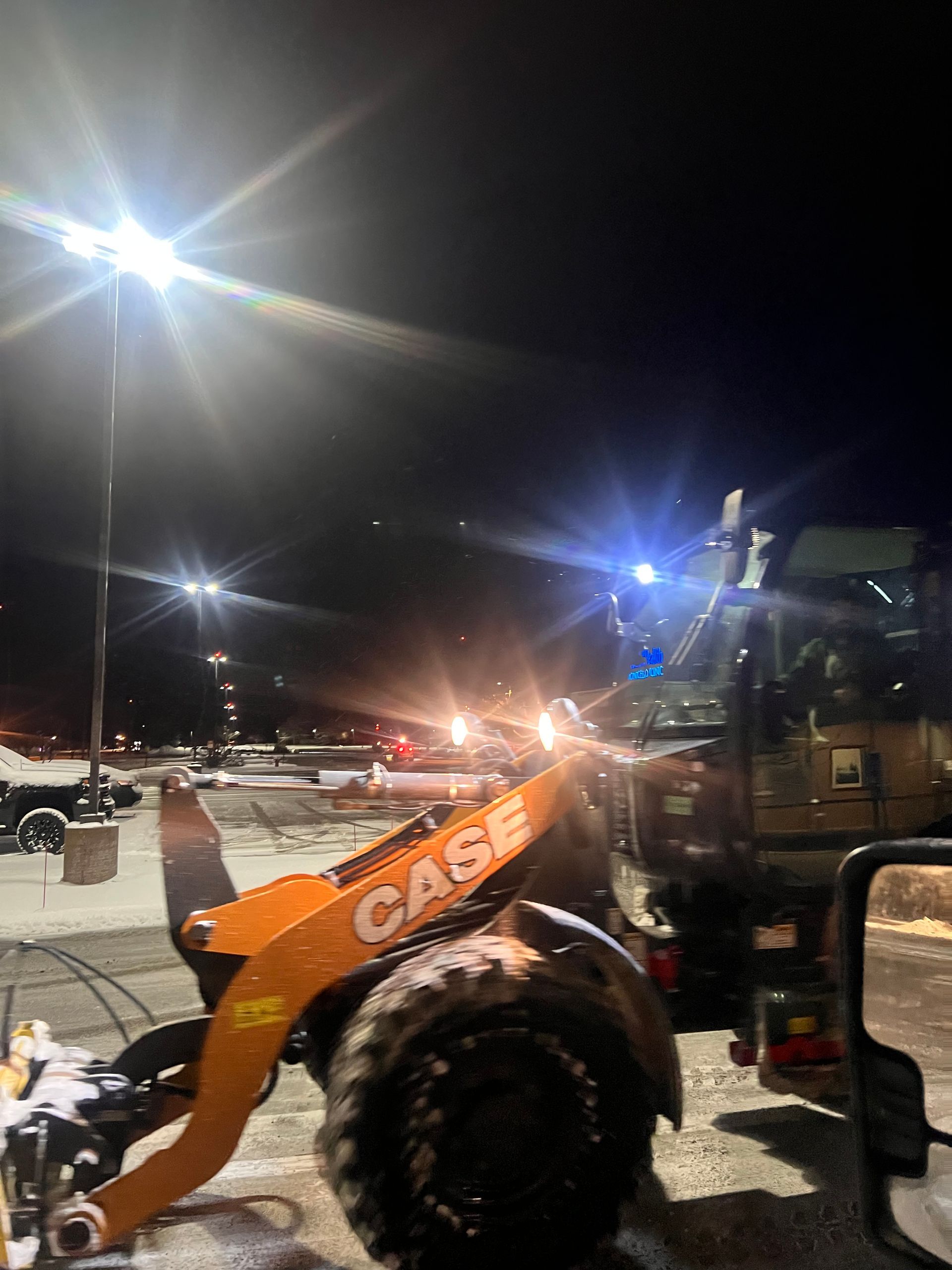 Orange CASE loader at a snowy construction site at night under bright lights