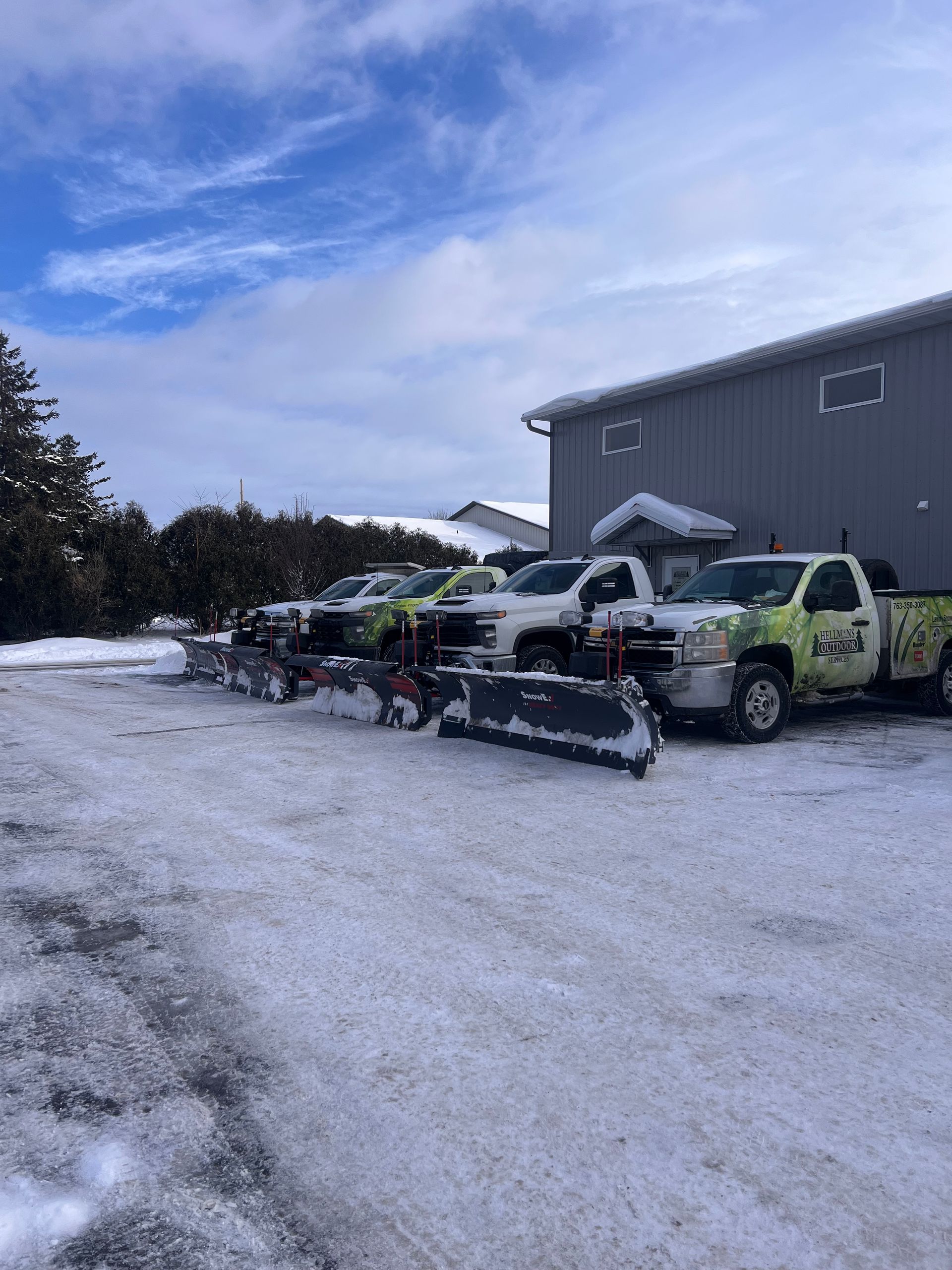 Snow-covered yard with parked vehicles and a gray building under a cloudy sky