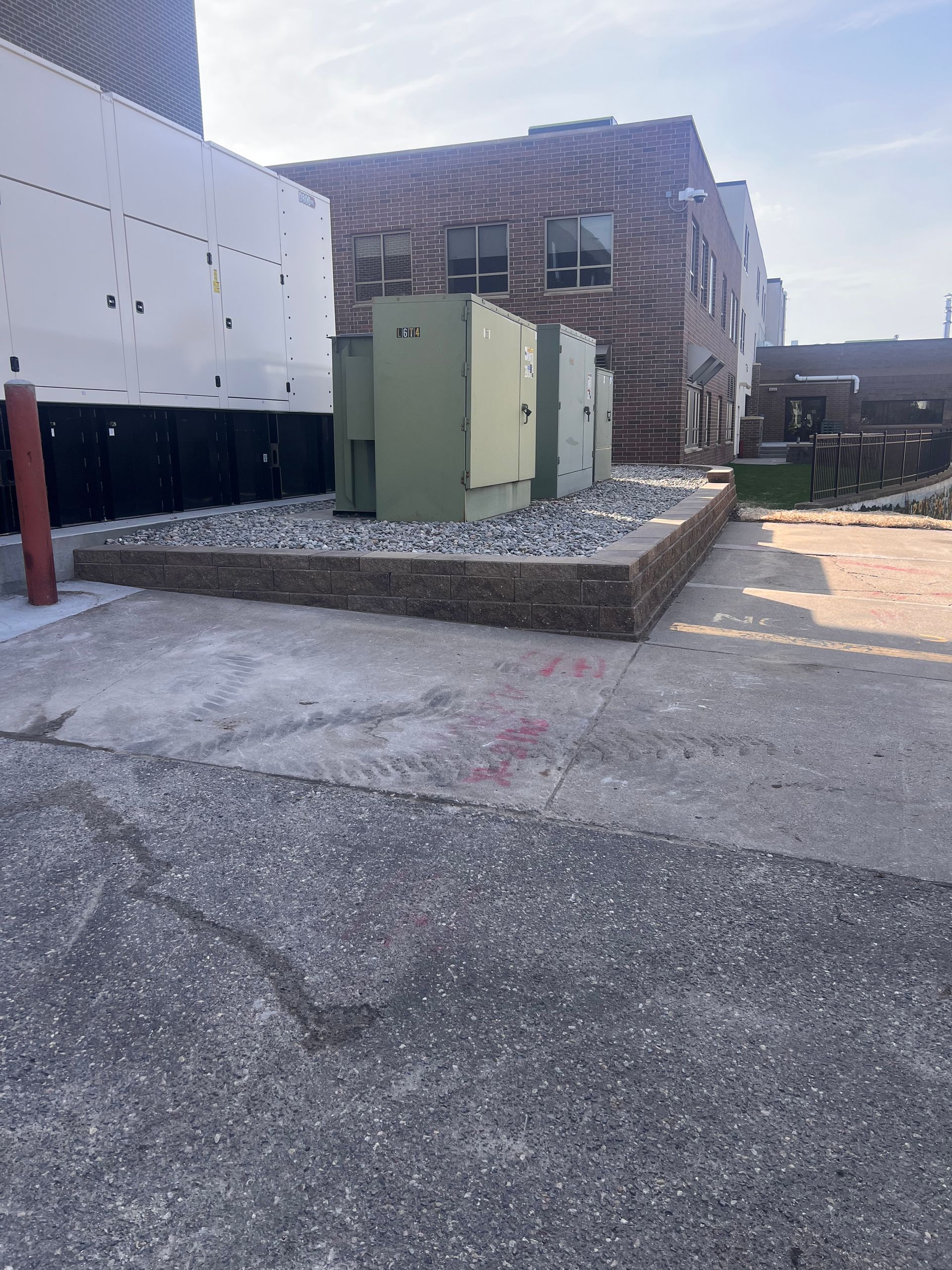 Construction site with green utility boxes beside a brick building and paved road