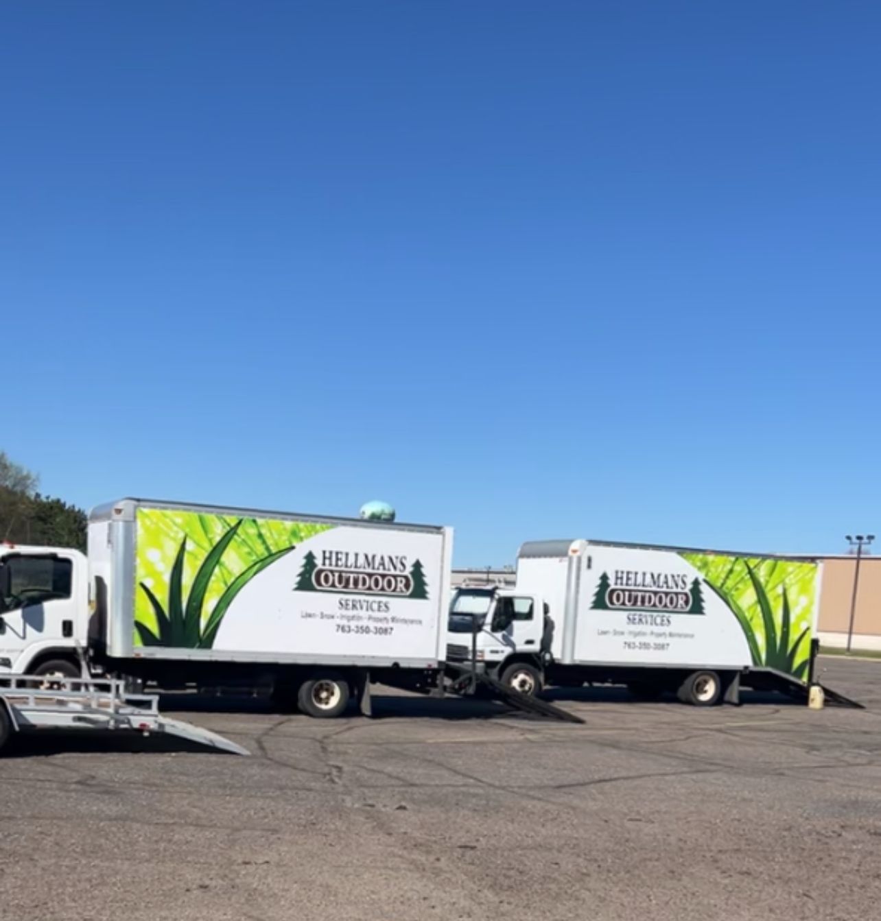 Two white moving trucks with green graphics parked in a lot under a clear blue sky