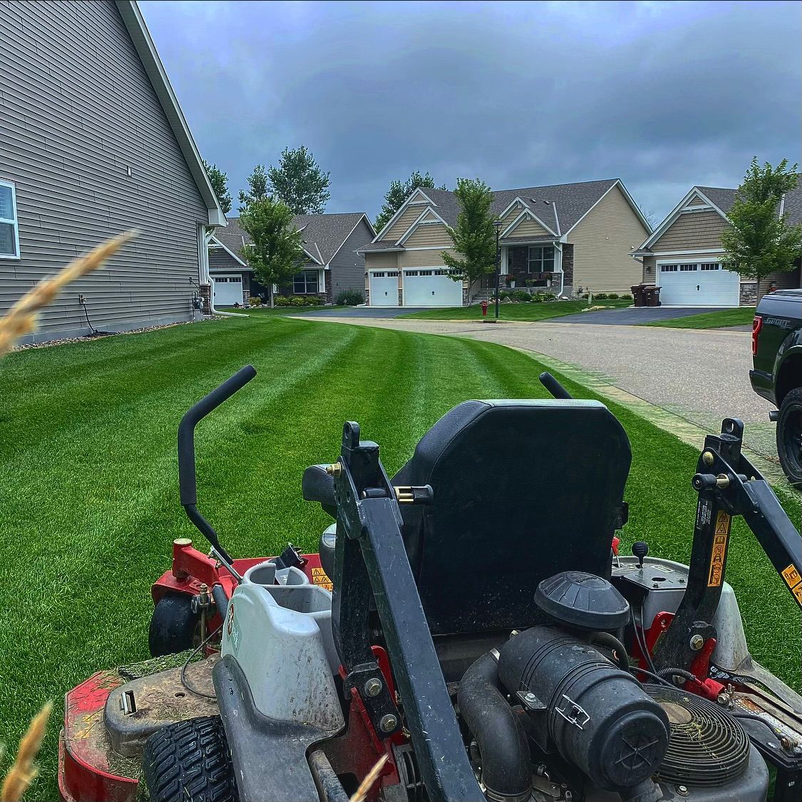 Lawn mower on a green suburban lawn with houses and cloudy sky in the background