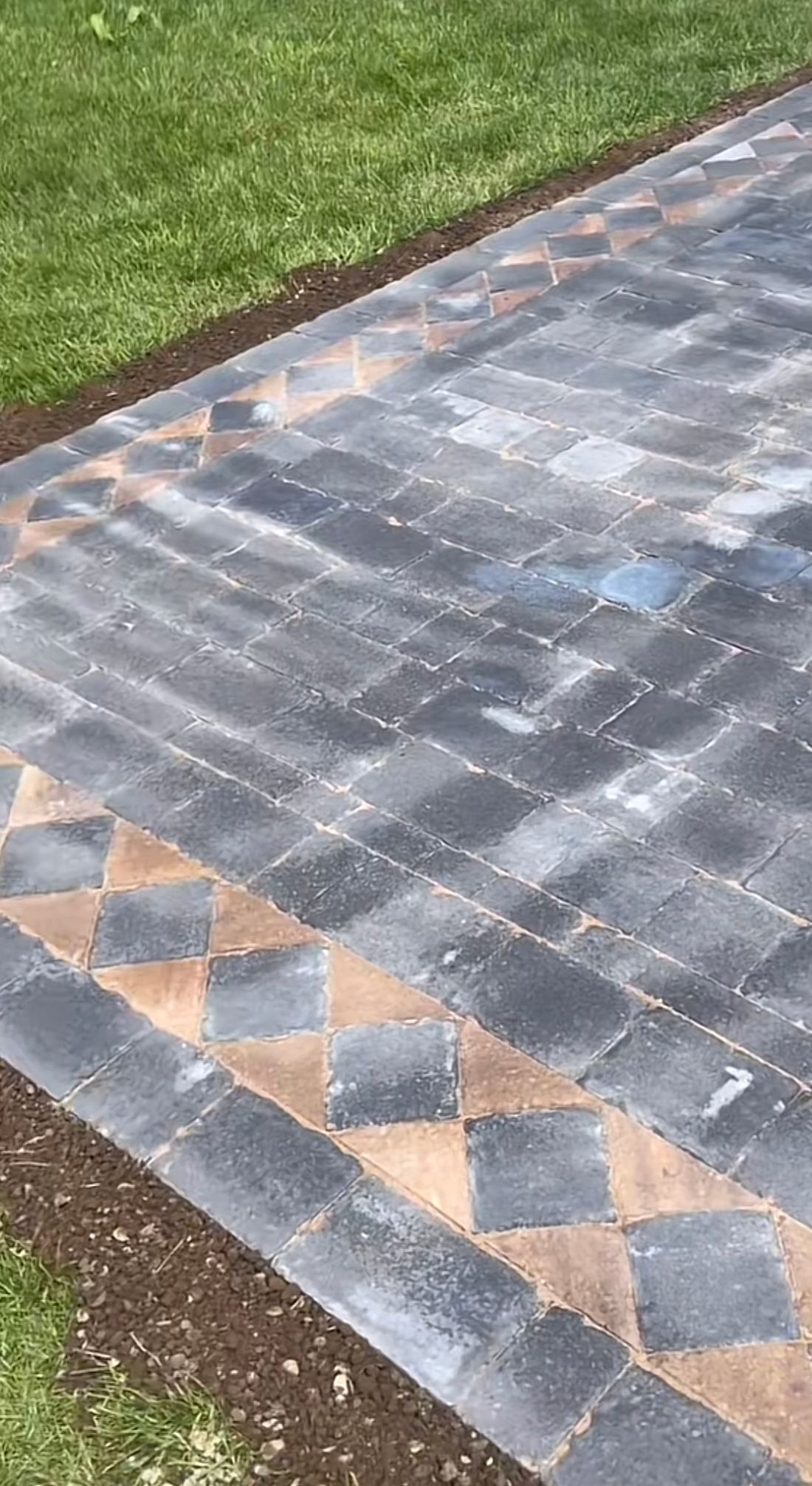 Patterned gray and tan paving stones beside a grassy lawn