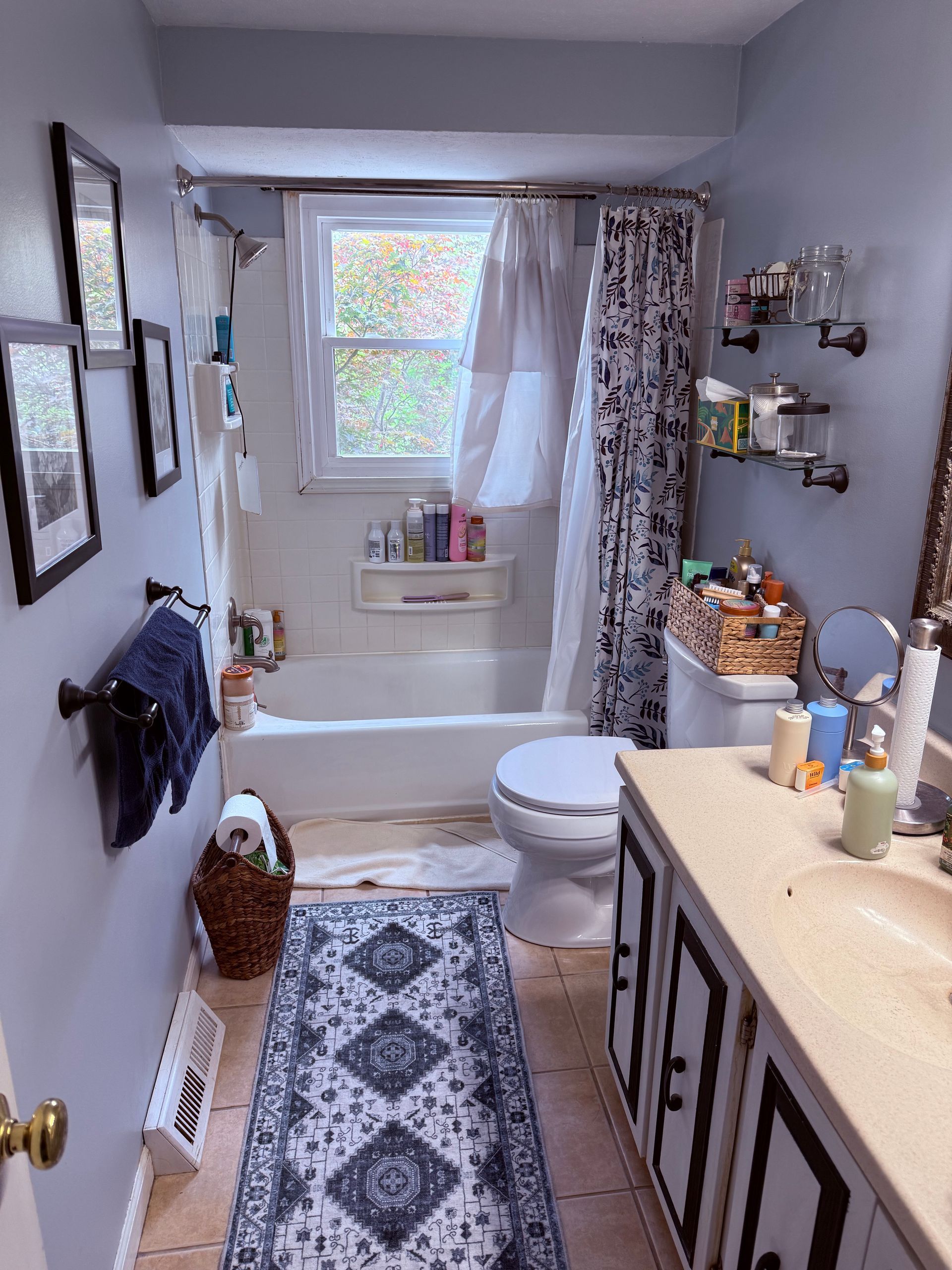 Narrow bathroom with white tub, toilet, patterned rug, gray walls, and light coming through the window.