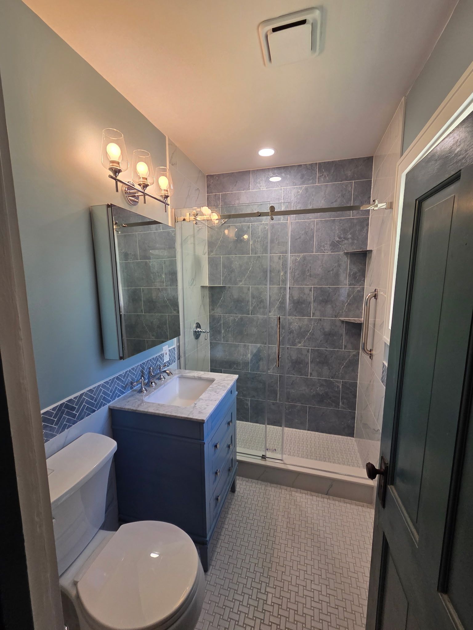 Small bathroom with toilet, vanity, mirror, and glass shower in gray and blue tones