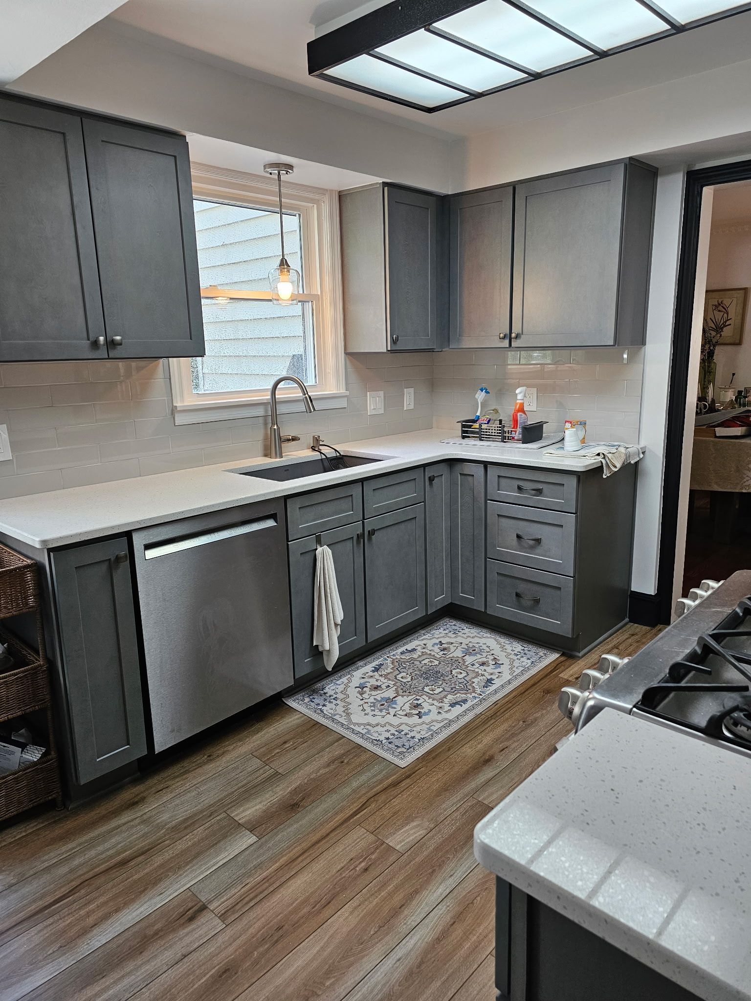 Modern kitchen with gray cabinets, stainless appliances, wood floors, and a sink under a window