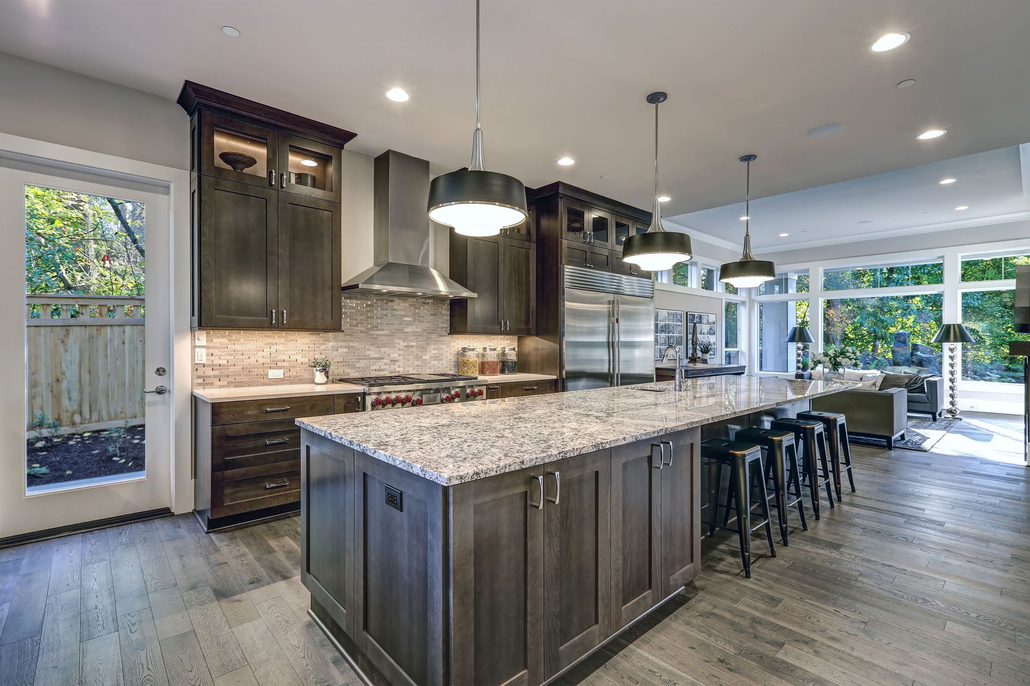 Modern kitchen with dark wood cabinets, large island, stainless steel appliances, and large windows.