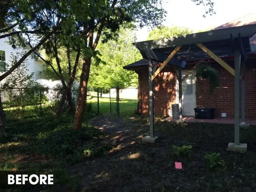 Backyard area with a brick house, a pergola, trees, and bare soil marked 