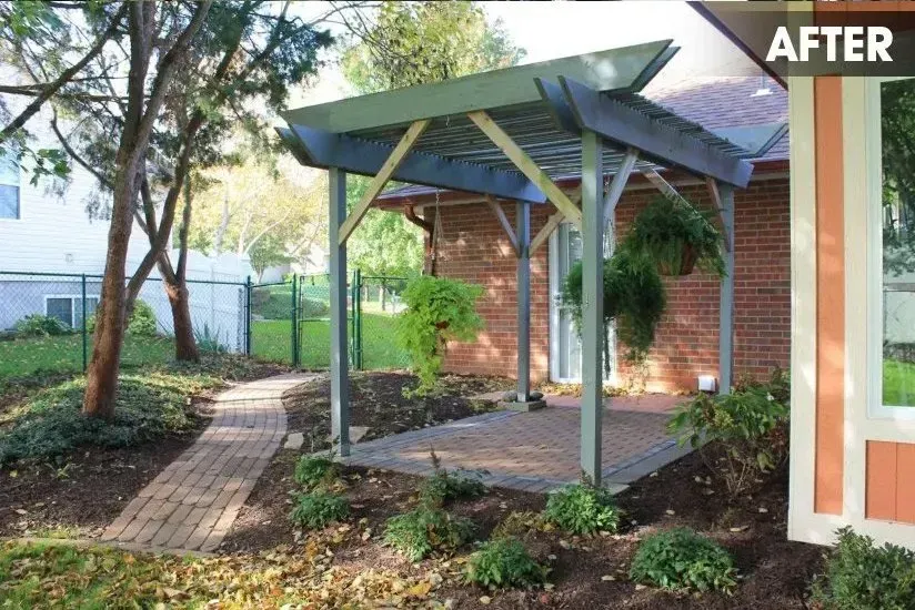 A brick patio with a pergola attached to a brick home, featuring a curved brick walkway through a landscaped garden.