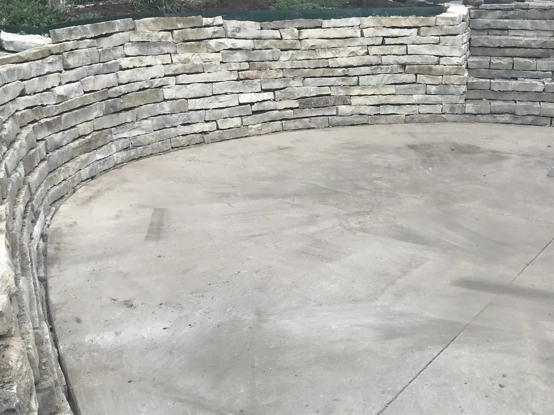 A curved, dry-stacked stone retaining wall surrounding a smooth, semi-circular concrete patio.