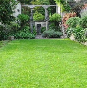 A green lawn leads to a stone garden archway and lush greenery in a park-like setting.