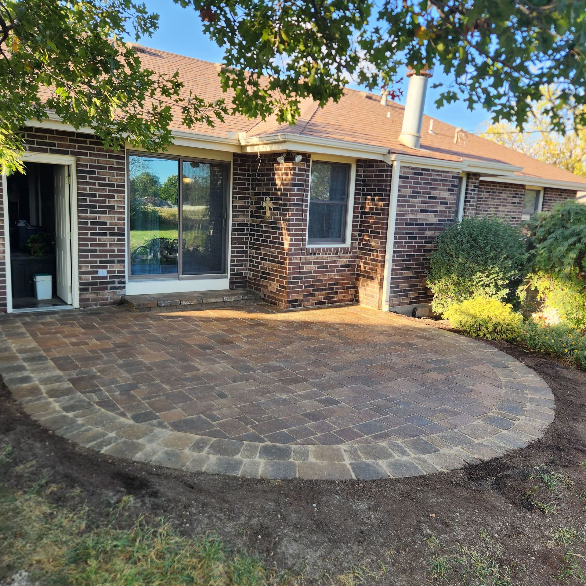 A newly installed curved brick paver patio in front of a brick house with a sliding glass door and windows.