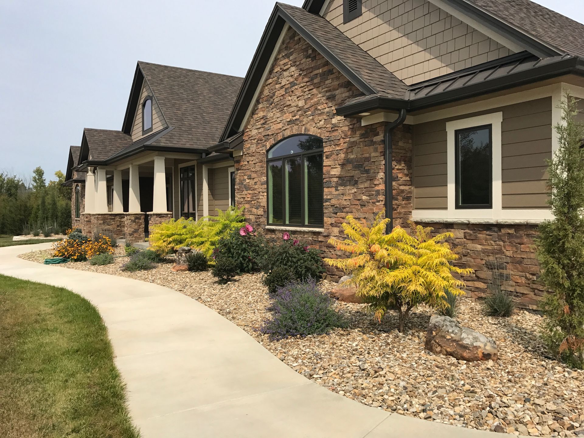 A concrete walkway leads past stone-accented residential buildings surrounded by decorative shrubs and gravel landscaping.