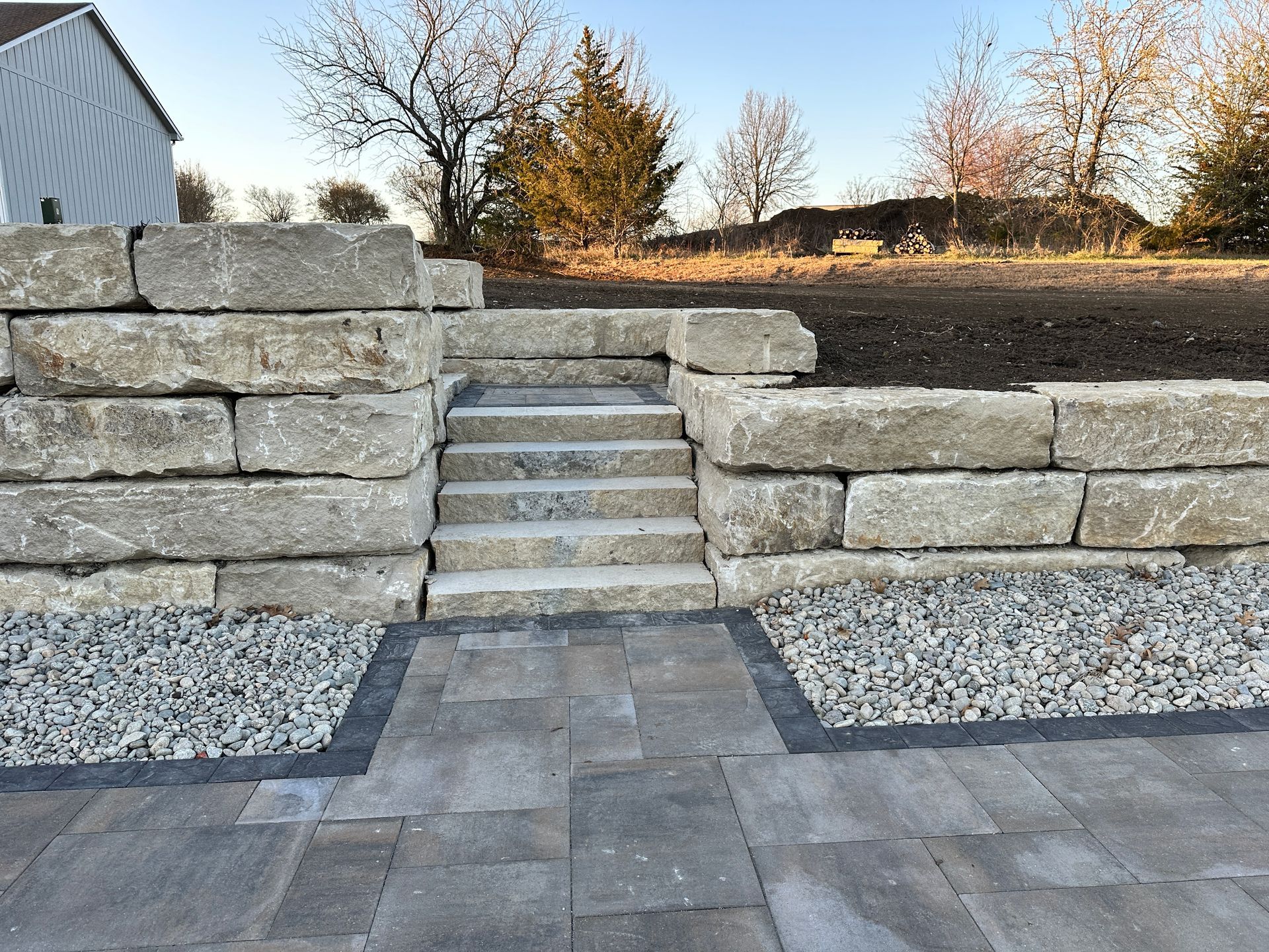 A set of natural stone steps built into a retaining wall, leading from a paver patio to an upper yard area.