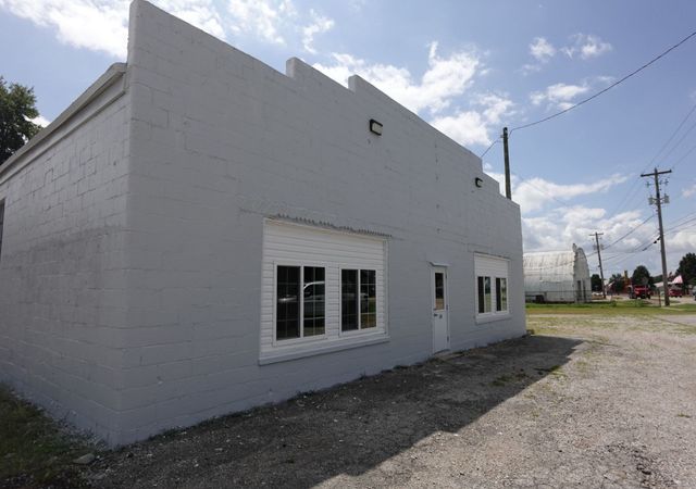 White stucco building with small windows on a gravel lot under a partly cloudy sky