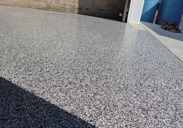 Textured gray speckled concrete floor beside a building wall in bright sunlight