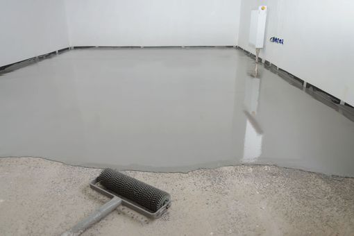 Wet concrete floor being smoothed with a squeegee in an empty room