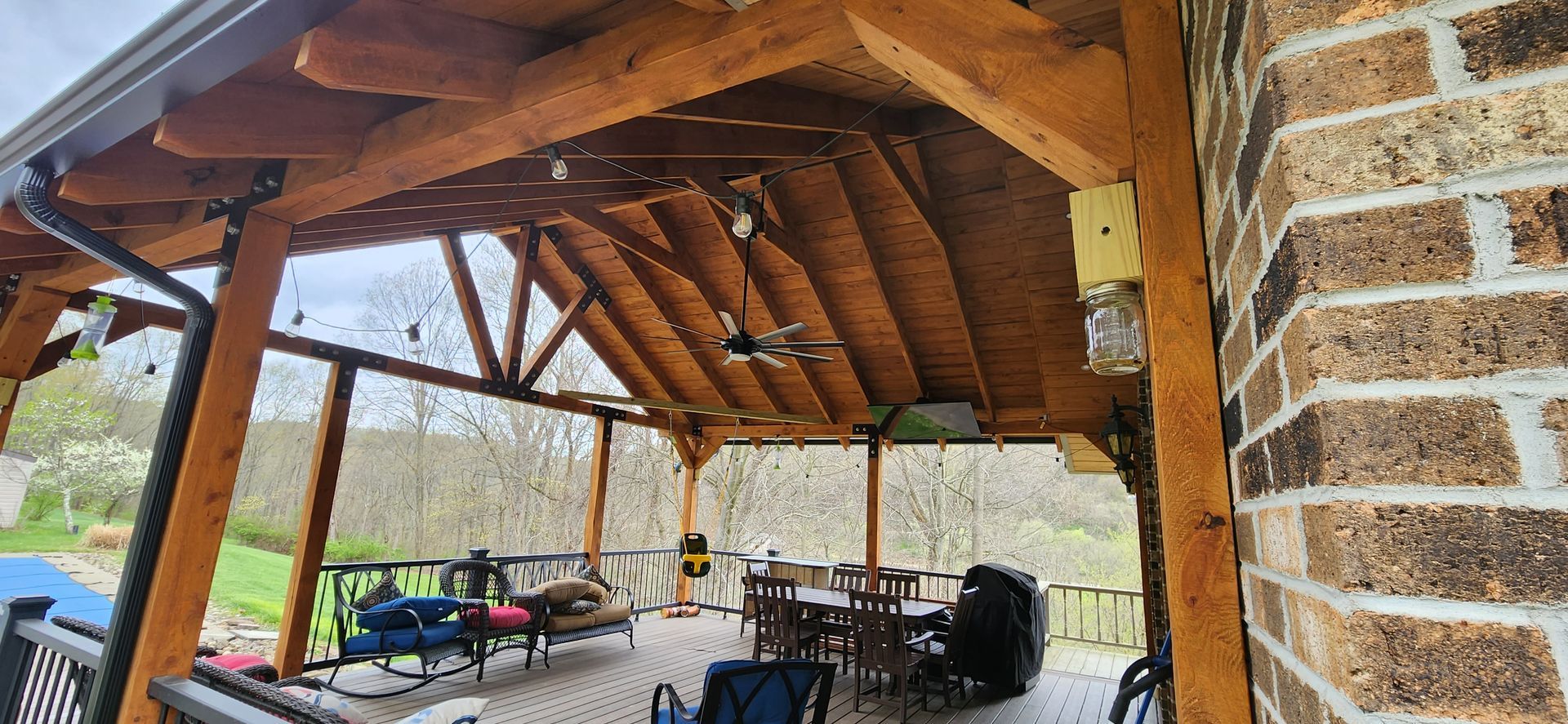 A wooden porch with a brick wall and a table and chairs underneath it.