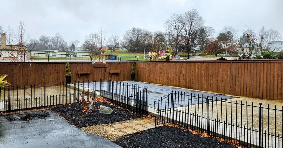A backyard with a wooden fence and a metal fence on a cloudy day.