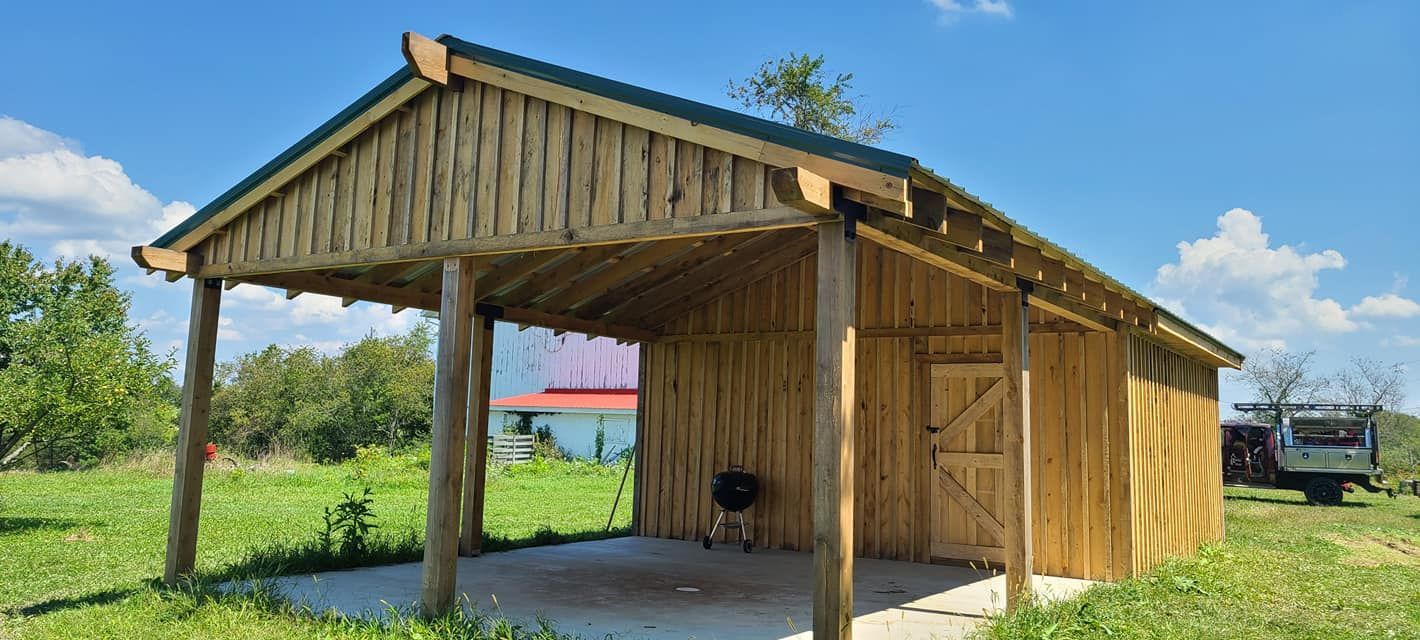 A wooden shed with a green roof is sitting in the middle of a grassy field.