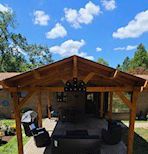 A wooden gazebo is sitting in front of a house on a sunny day.