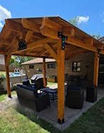 A wooden pergola with furniture underneath it in a backyard.